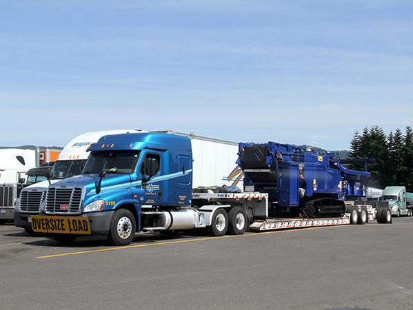 blue flatbed semi truck towing heavy equipment